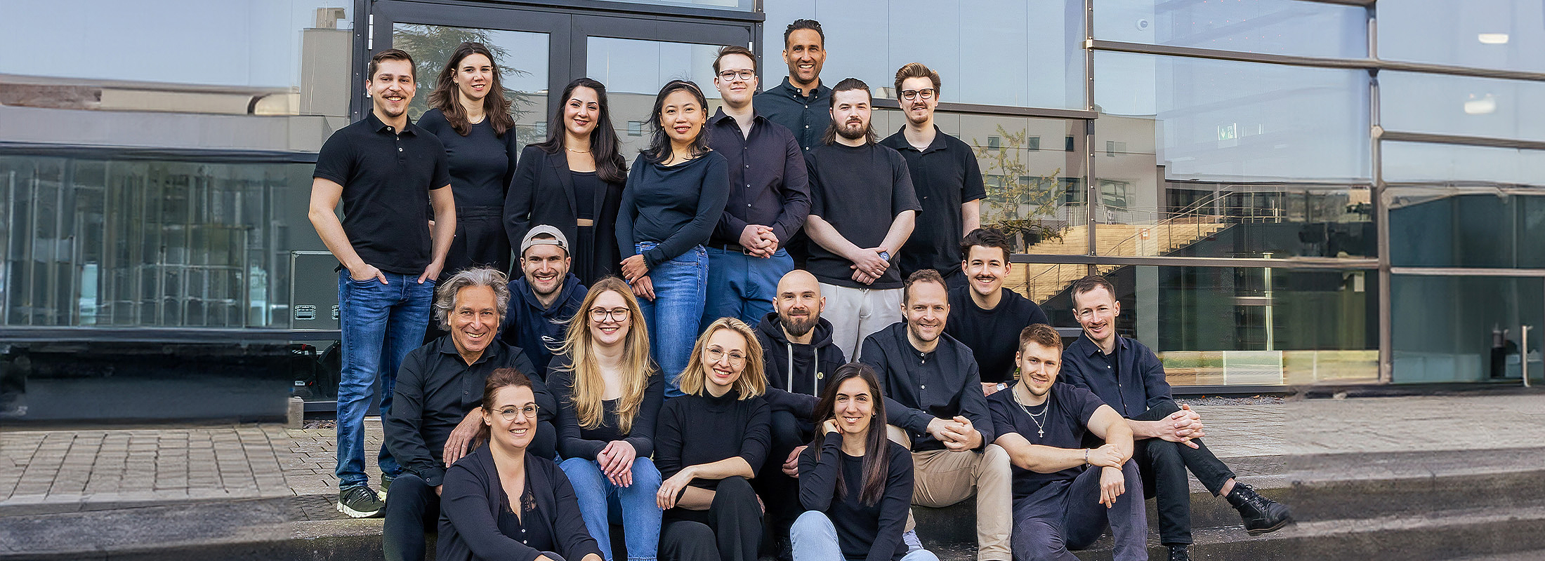 Gruppenfoto des mindtwo Teams auf einer Außentreppe, alle in schwarzer Kleidung, lächelnd in die Kamera