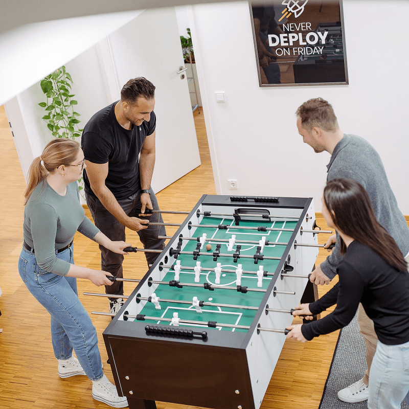 Vier mindtwo Teammitglieder spielen gemeinsam Tischkicker im B&uuml;ro